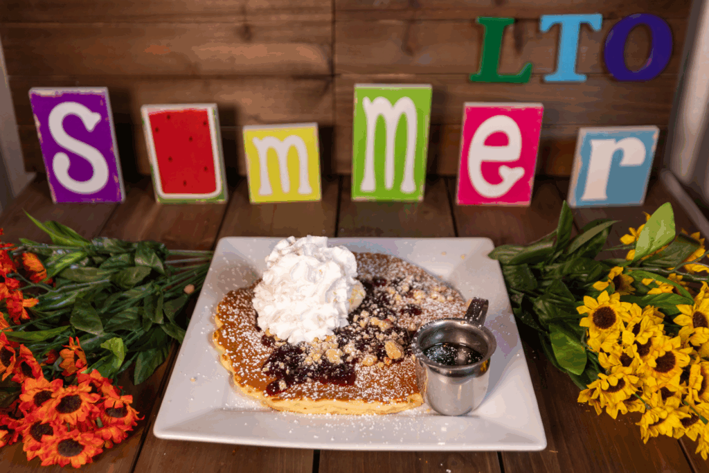 Close-up of a giant blueberry pie pancake from Hash House A Go Go, topped with whipped cream, blueberry compote, and powdered sugar—part of their signature twisted farm food menu.