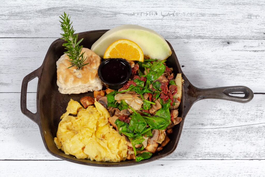 Vegetarian scramble with fresh eggs, bell peppers, spinach, tomatoes, and onions, served with crispy potatoes and a biscuit at Hash House A Go Go Henderson.